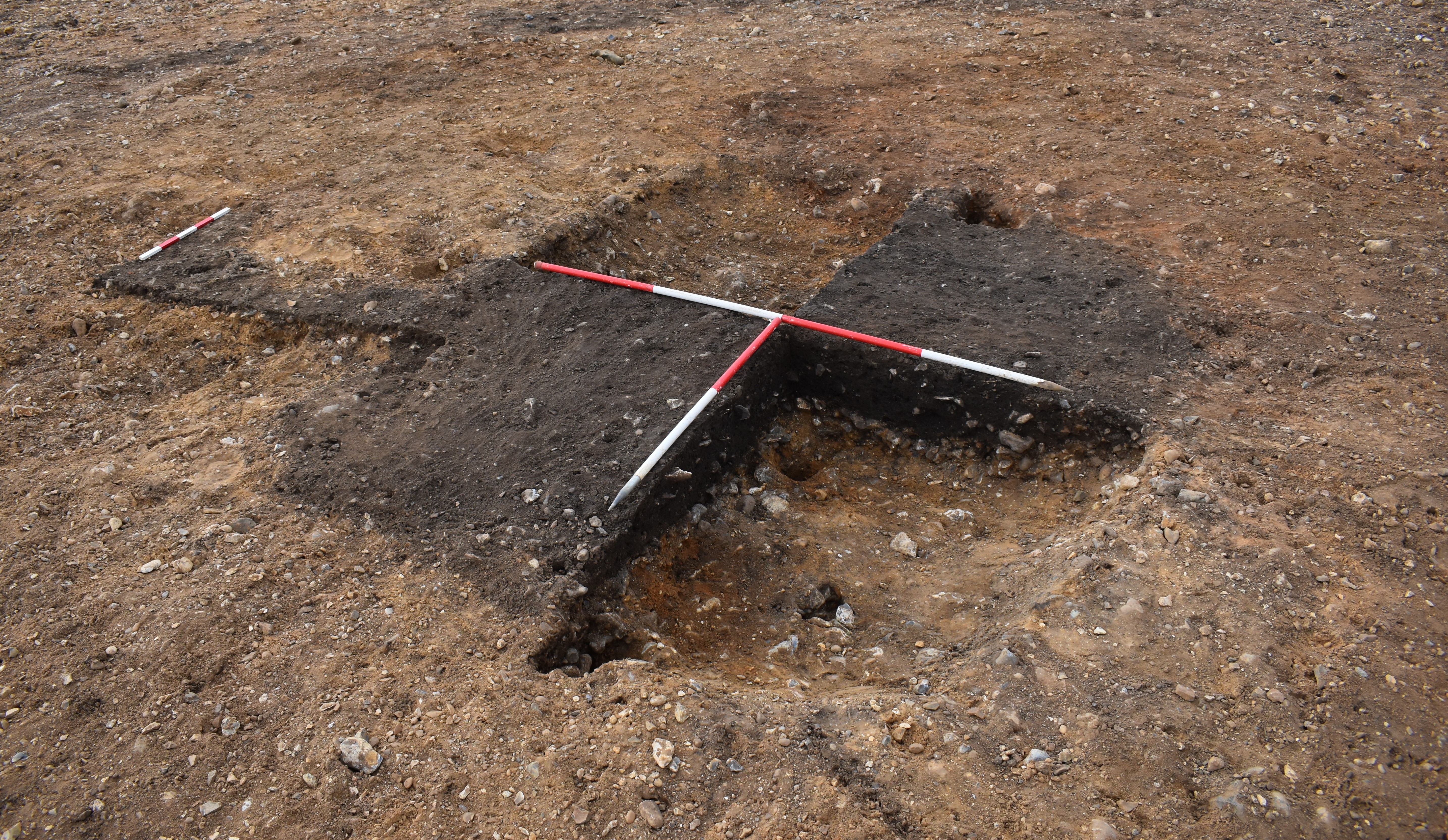 A dark rectangular circle in the middle of lighter brown soil. Archaeologists have dug out 2 quarters to show the depth.