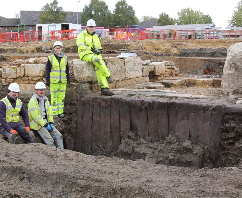 Image with the OA team posing with remains of a timber structure from the Westgate site in Oxford. 